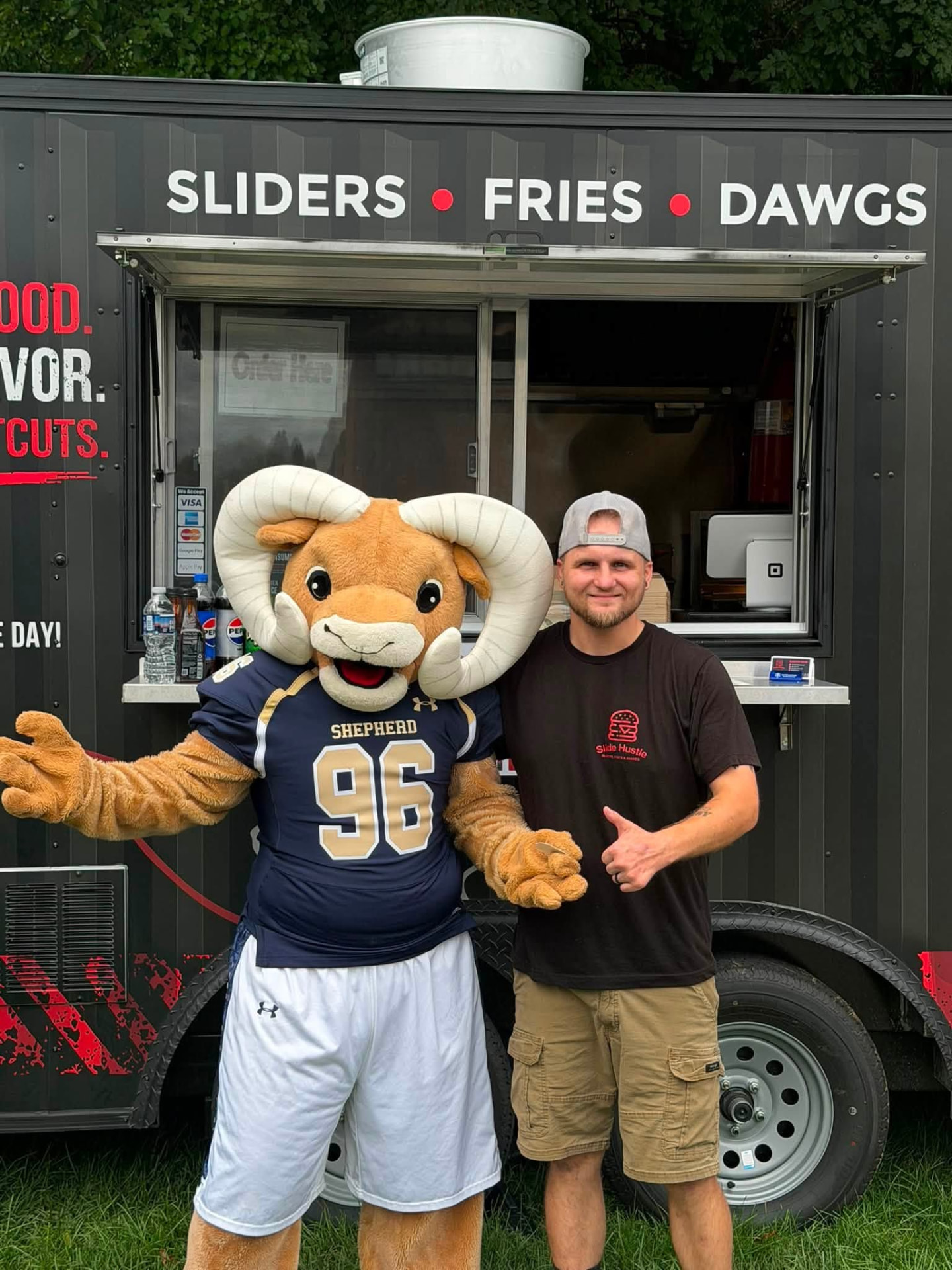 A man and the Shepherd ram mascot outside the Slide Hustle food truck